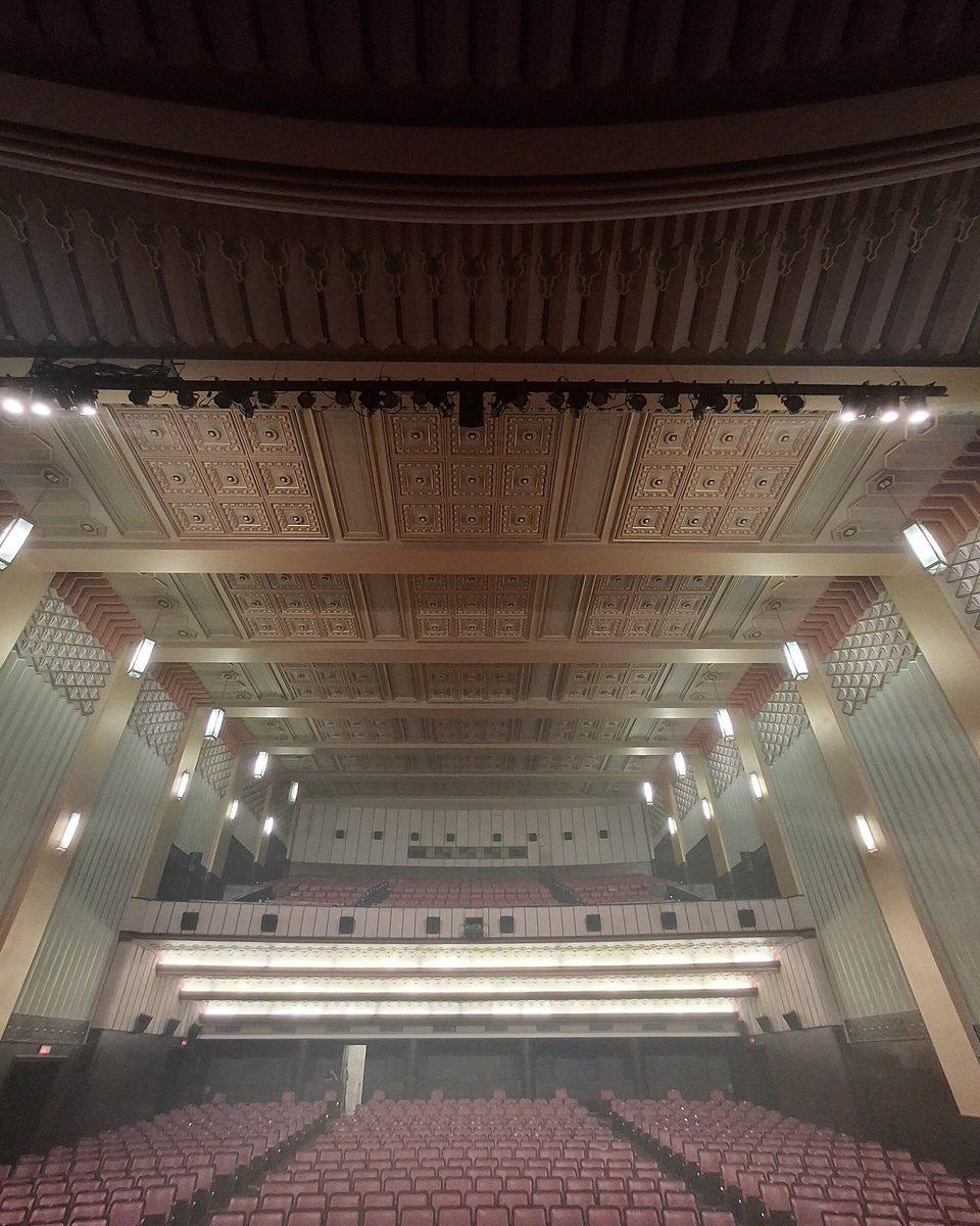 Sala do Cineteatro São Luiz, em Fortaleza, vista a partir do palco, com fileiras de poltronas vermelhas, o balcão ao fundo e o teto art déco com frisos e luminárias nas paredes.