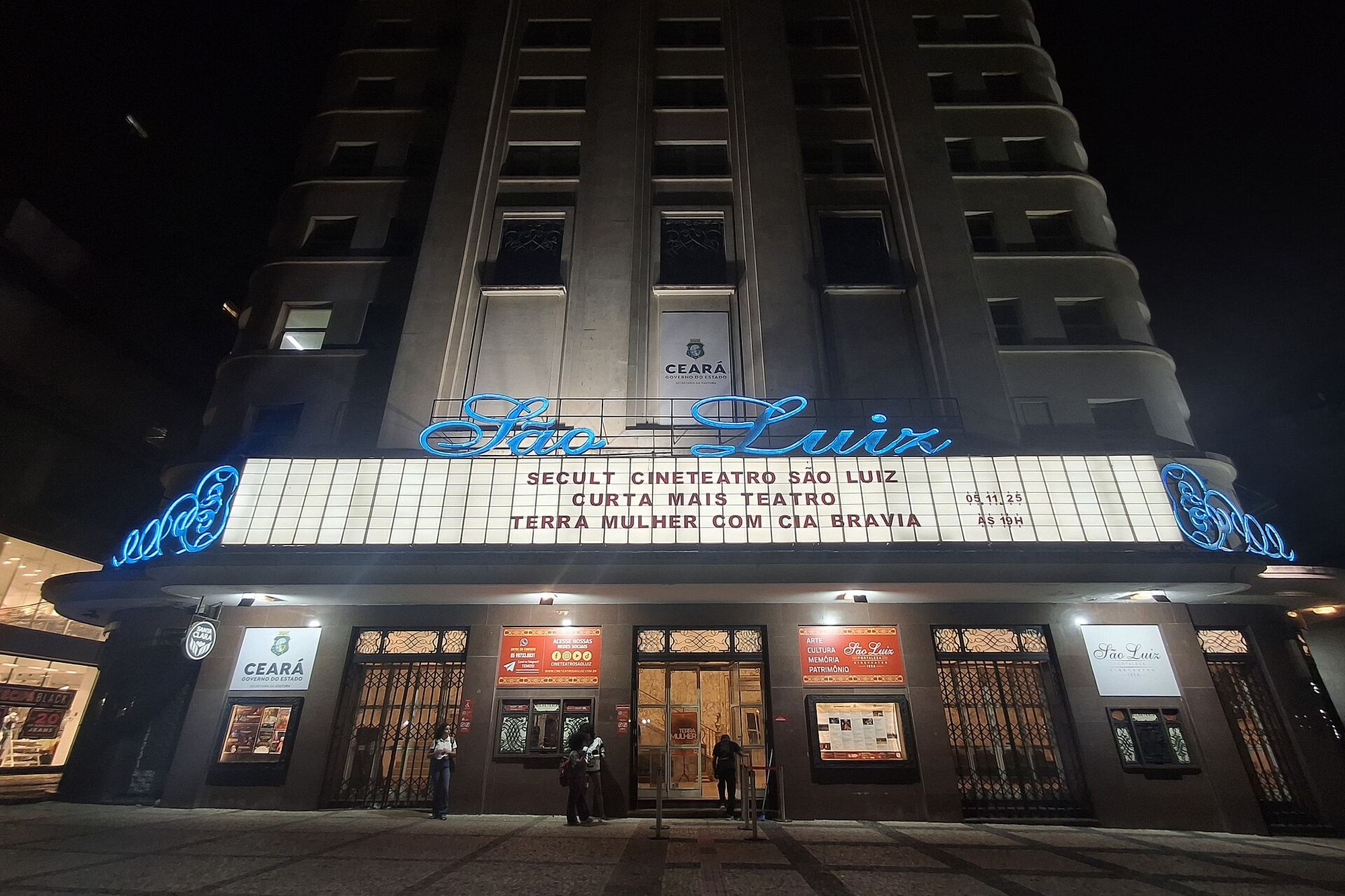 Fachada do Cineteatro São Luiz à noite, na Praça do Ferreira, no Centro de Fortaleza, com o letreiro iluminado em azul e a marquise com a programação acesa sobre as portas de entrada.