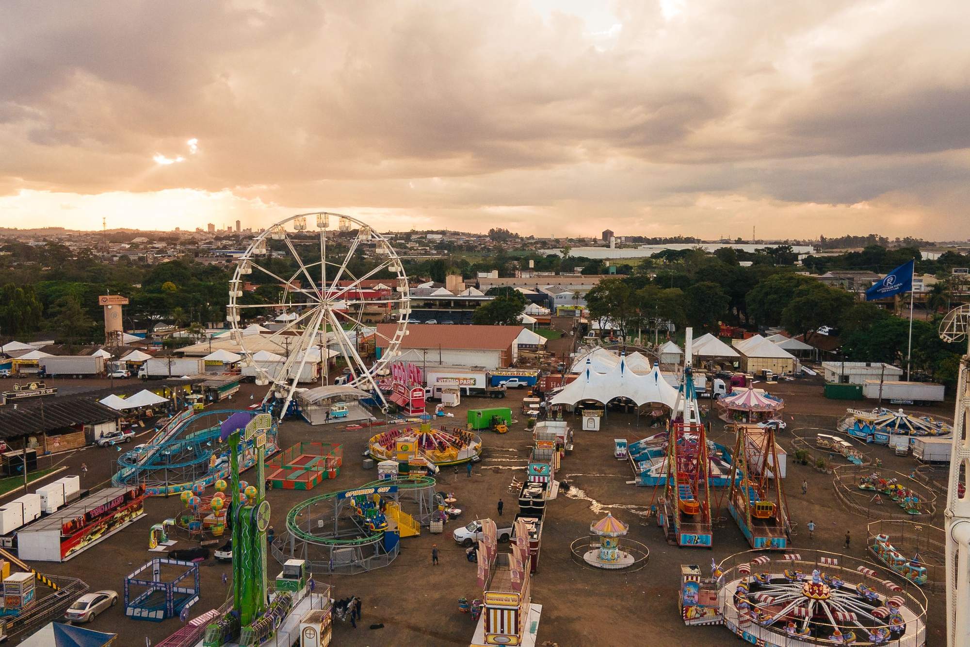 Vista aérea do parque de diversões da ExpoLondrina ao entardecer, com a roda-gigante e a cidade ao fundo.