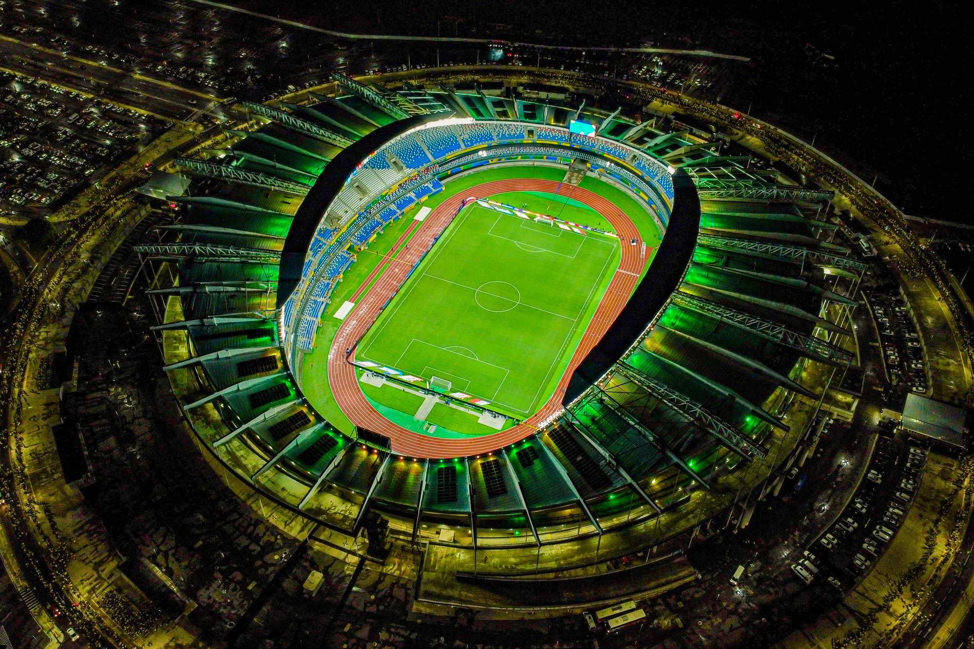 Vista aérea noturna do Estádio Olímpico do Pará, o Mangueirão, em Belém, com o anel de arquibancadas iluminado e o gramado no centro.