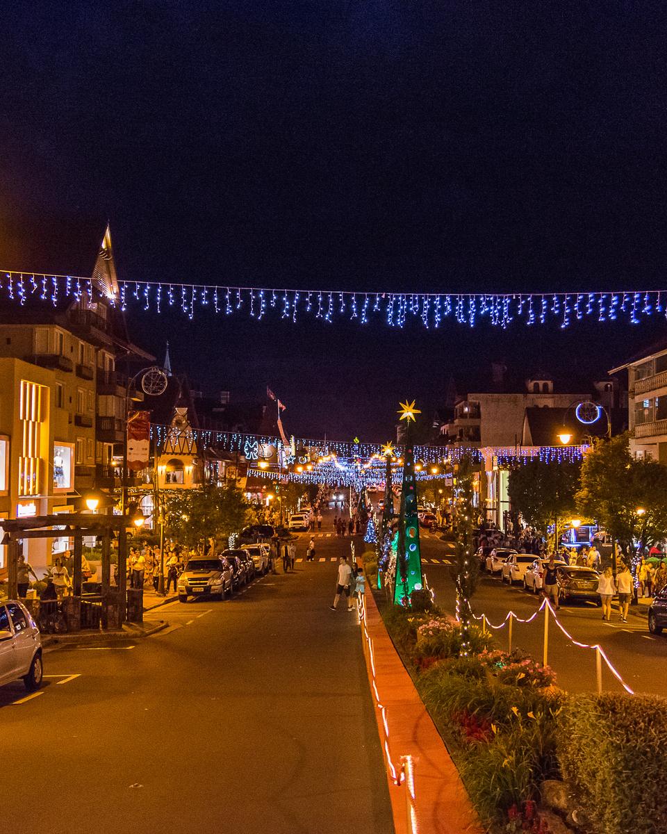Avenida Borges de Medeiros, em Gramado, à noite com a decoração de Natal acesa e gente passeando pela calçada.