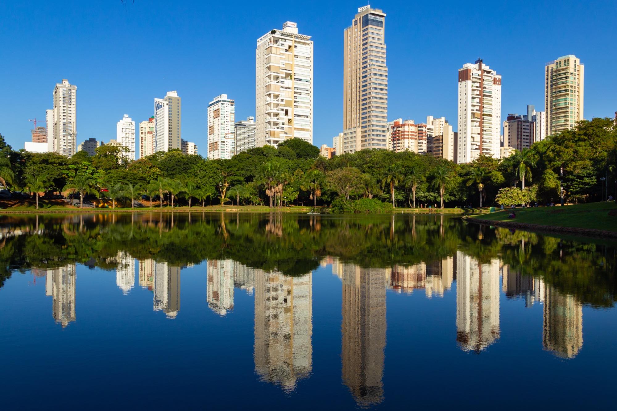 Lago do Parque Vaca Brava, em Goiânia, com os prédios do Setor Bueno refletidos na água em fim de tarde de céu azul.