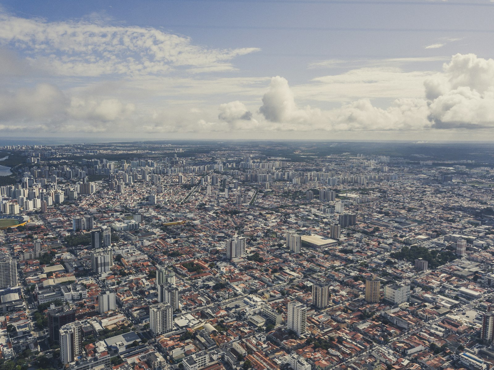 Vista aérea da cidade de Aracaju, com prédios altos, ruas em quadras e nuvens no horizonte.