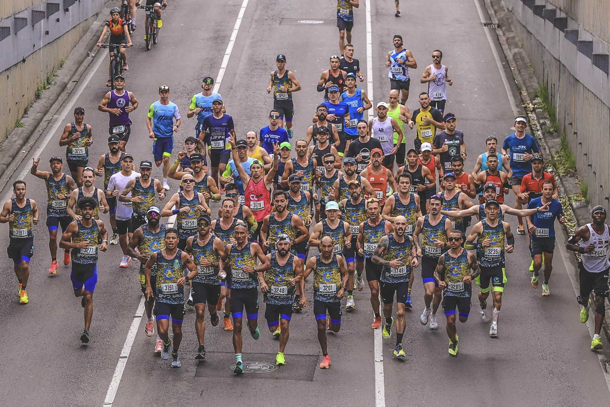 Pelotão de corredores da Maratona de Curitiba descendo uma passagem de concreto.