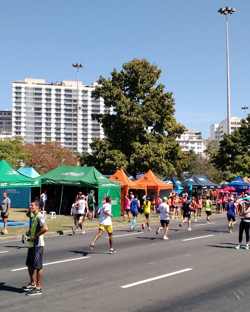 Corredores passando por uma fileira de tendas coloridas de assessorias esportivas montadas no gramado do Aterro do Flamengo, no Rio de Janeiro, durante a Meia Maratona Internacional do Rio de 2015.