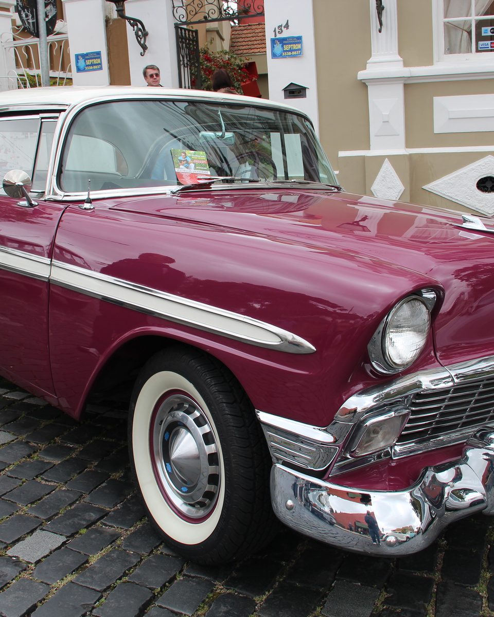 Chevrolet Bel Air de 1956, vinho e branco, com cromados polidos e pneus de faixa branca, estacionado numa rua de paralelepípedos de Curitiba durante uma exposição de carros antigos.