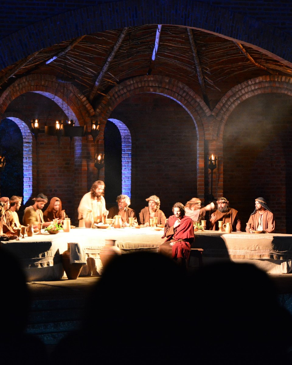 Cena da Santa Ceia no Cenáculo de Nova Jerusalém, à noite: atores em trajes de época em volta de uma mesa longa, sob arcos de tijolo iluminados por tochas, com a cabeça da plateia em silhueta no primeiro plano.
