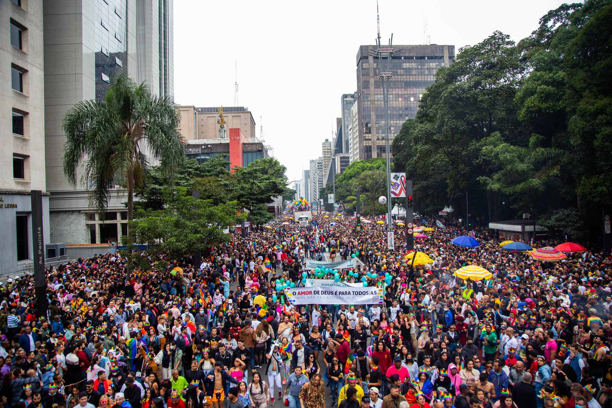 Multidão com bandeiras e adereços de arco-íris ocupando a Avenida Paulista, vista do alto, durante a Parada do Orgulho LGBT+ de São Paulo de 2022.