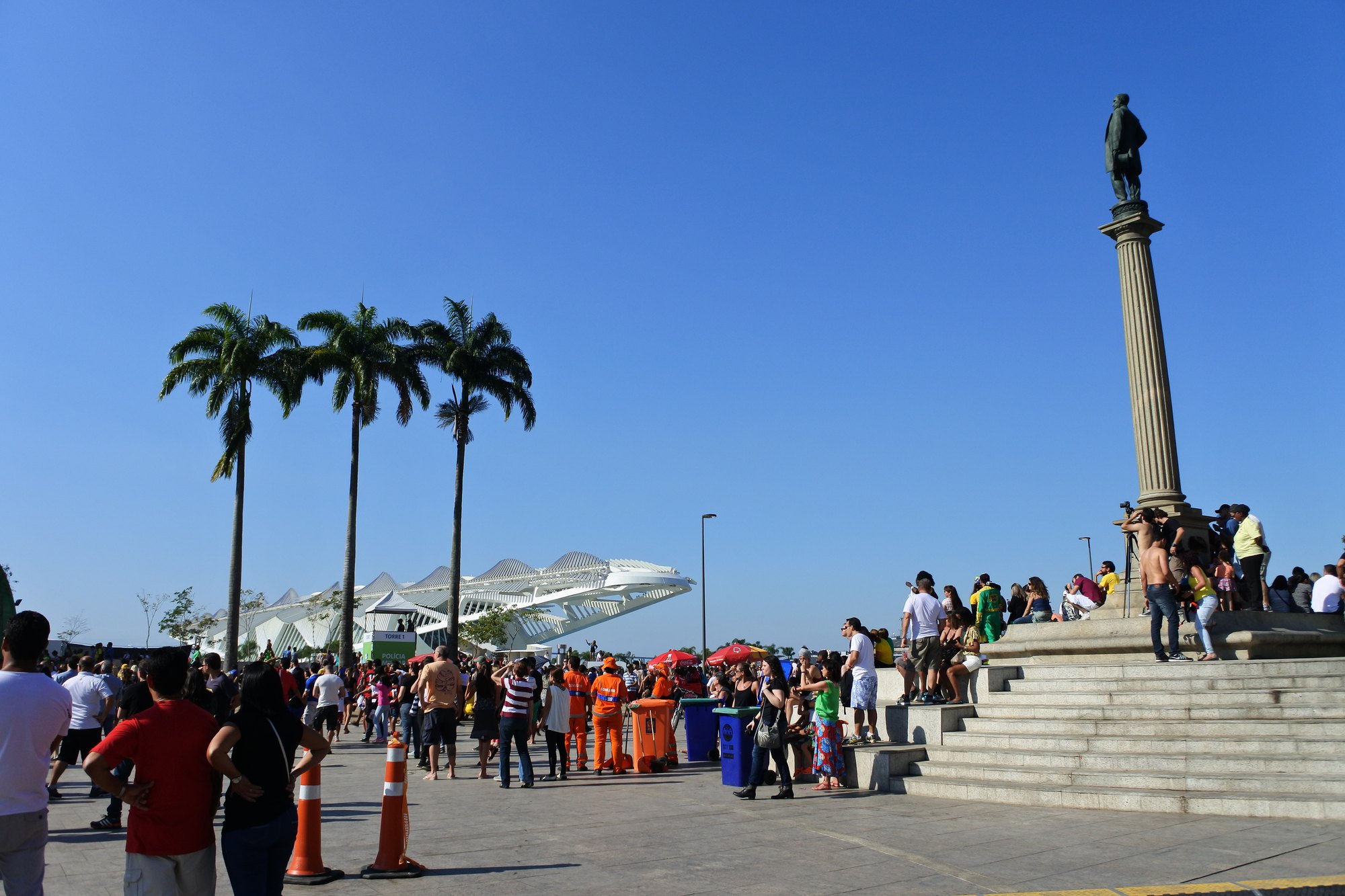 Público circula pela Praça Mauá, no Centro do Rio de Janeiro, com o Museu do Amanhã e palmeiras ao fundo e a coluna com a estátua do Barão de Mauá à direita.