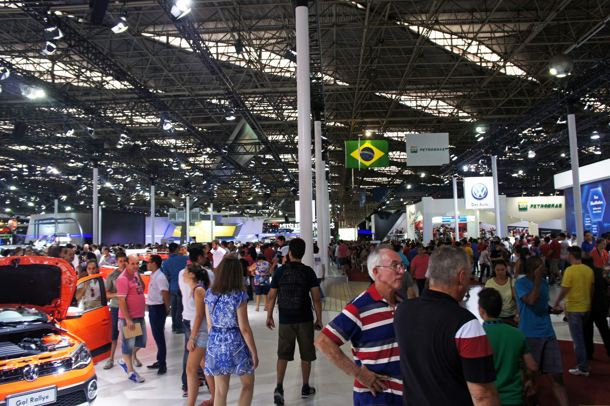 Corredor central do pavilhão do Anhembi cheio de visitantes entre estandes de carros, com uma bandeira do Brasil pendurada no teto, no Salão Internacional do Automóvel de 2014, em São Paulo.
