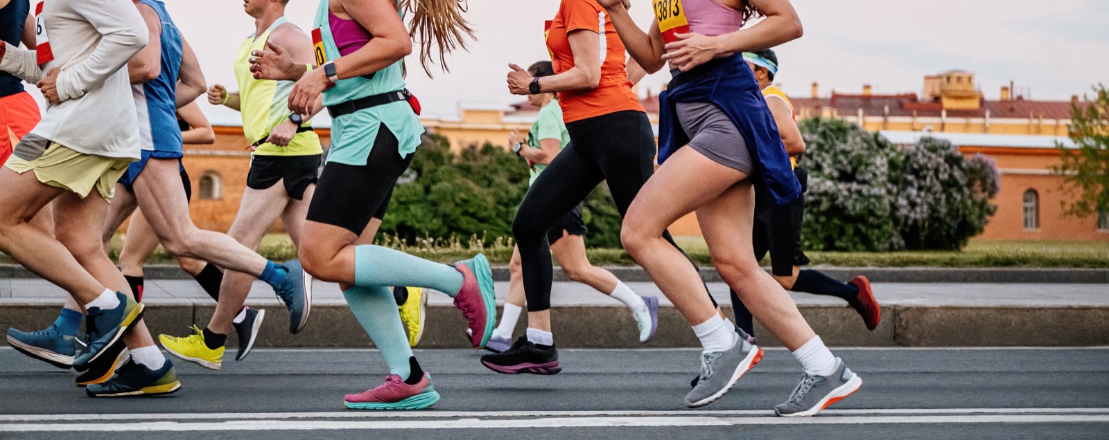 Grupo de corredores e corredoras de roupa colorida numa corrida de rua na cidade, em plena passada.