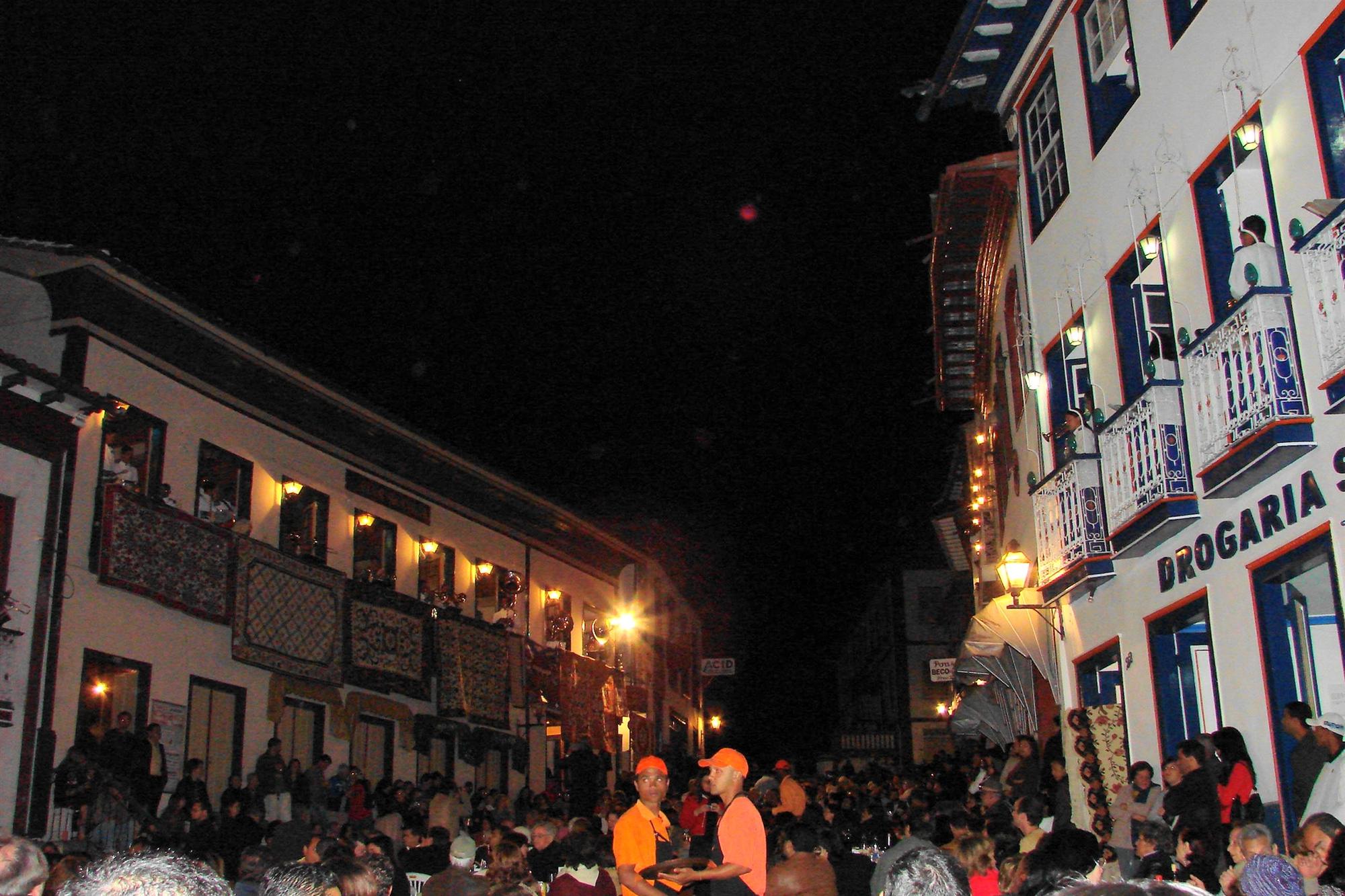 Rua da Quitanda lotada à noite durante a Vesperata, em Diamantina, com músicos nas sacadas iluminadas dos casarões coloniais e tapeçarias penduradas nos parapeitos.