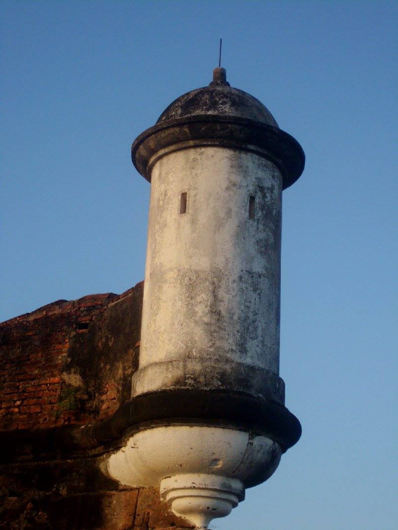 Garita de pedra e alvenaria no alto da muralha da Fortaleza de São José de Macapá, com céu azul ao fundo e luz de fim de tarde