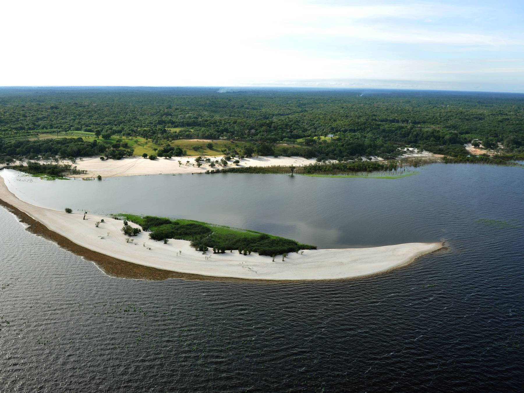Vista aérea da Praia da Lua em Manaus, com o banco de areia curvo cercado pela água escura do rio Negro e a floresta ao fundo