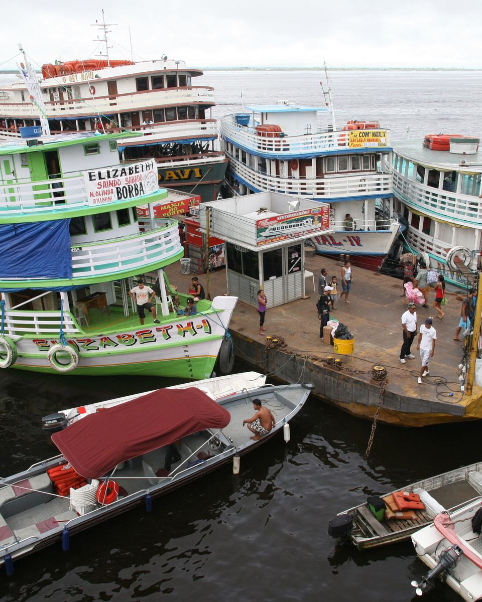 Porto Flutuante de Manaus com barcos regionais de dois andares atracados lado a lado, passageiros embarcando na plataforma e lanchas amarradas na frente.