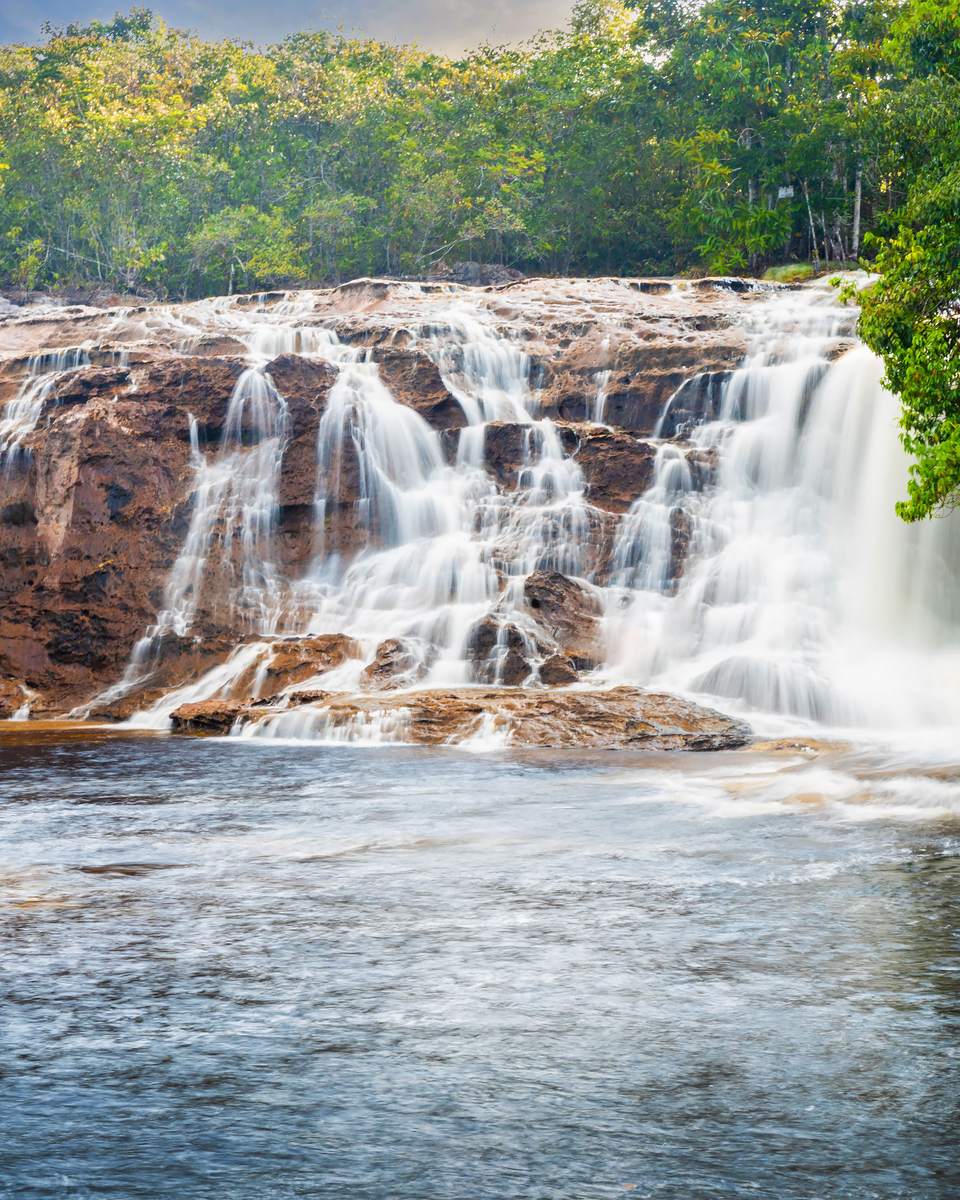 Cachoeira da Iracema, em Presidente Figueiredo, com a água caindo em cortina sobre a rocha avermelhada e a mata fechada nas duas margens.