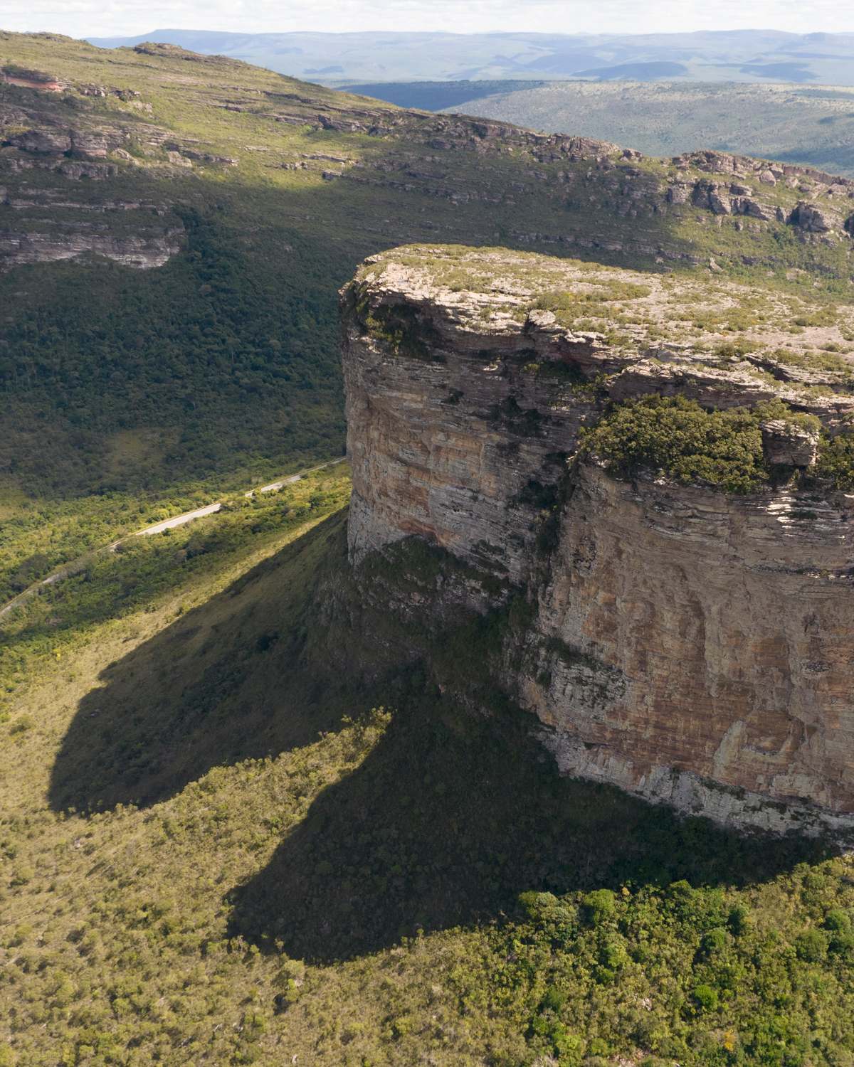Morro do Pai Inácio, de paredões de pedra e topo plano, visto do alto, com a estrada de terra ao pé e a vegetação da Chapada Diamantina até o horizonte.