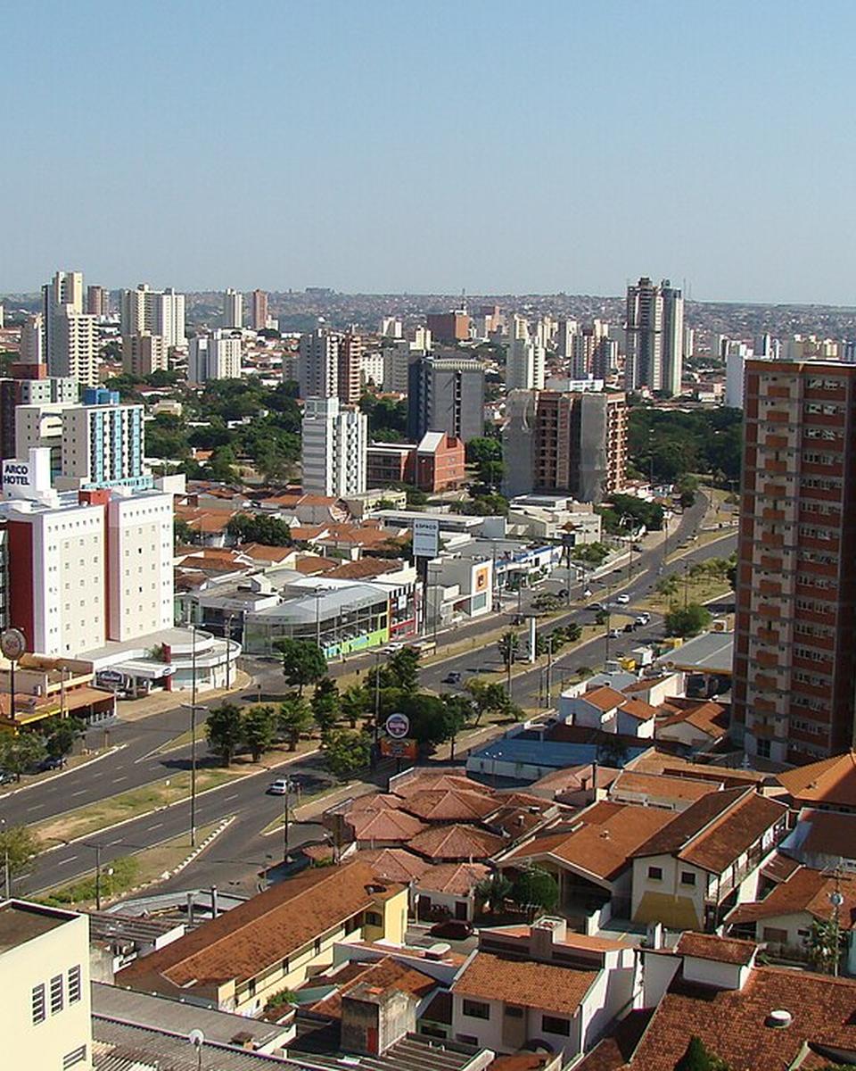 Vista do alto da região da Avenida Nações Unidas, em Bauru, com prédios residenciais, casas de telhado vermelho e a avenida arborizada cortando o bairro.