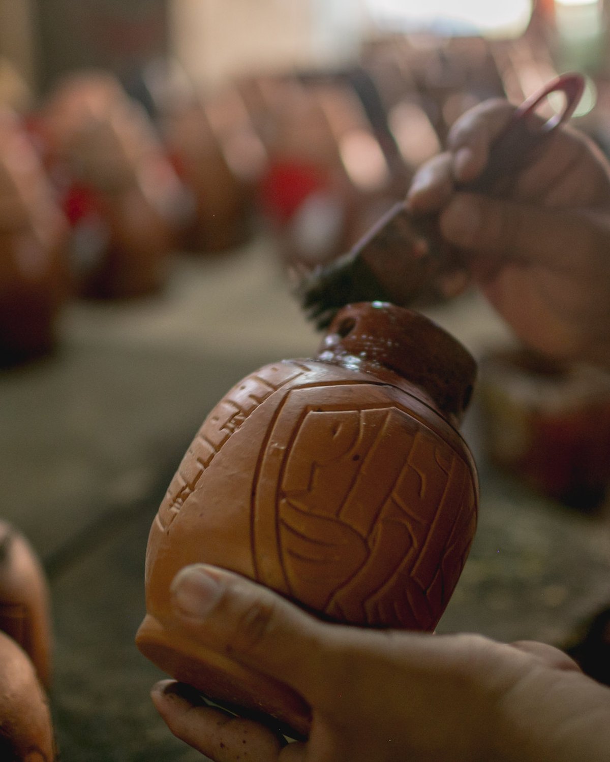 Mãos de artesã segurando um pote de barro com grafismo marajoara, numa bancada cheia de peças de cerâmica em Icoaraci.