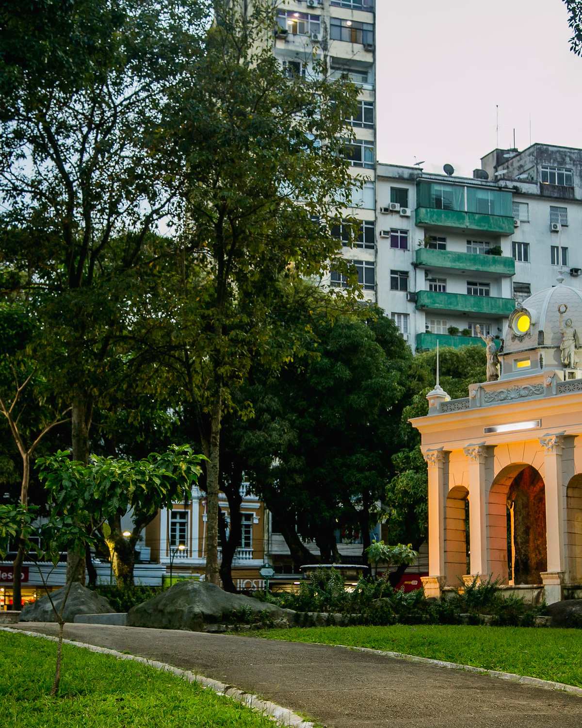 Coreto amarelo da Praça da República, em Belém, cercado de árvores altas e gramado, com prédios residenciais ao fundo.