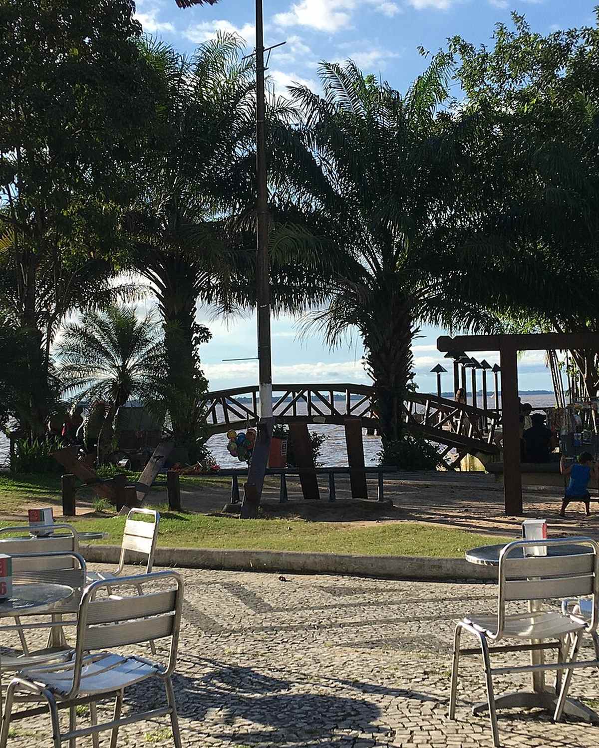 Mesas e cadeiras do Ver-o-Rio sob as palmeiras, com pessoas sentadas de frente para a baía do Guajará, em Belém.