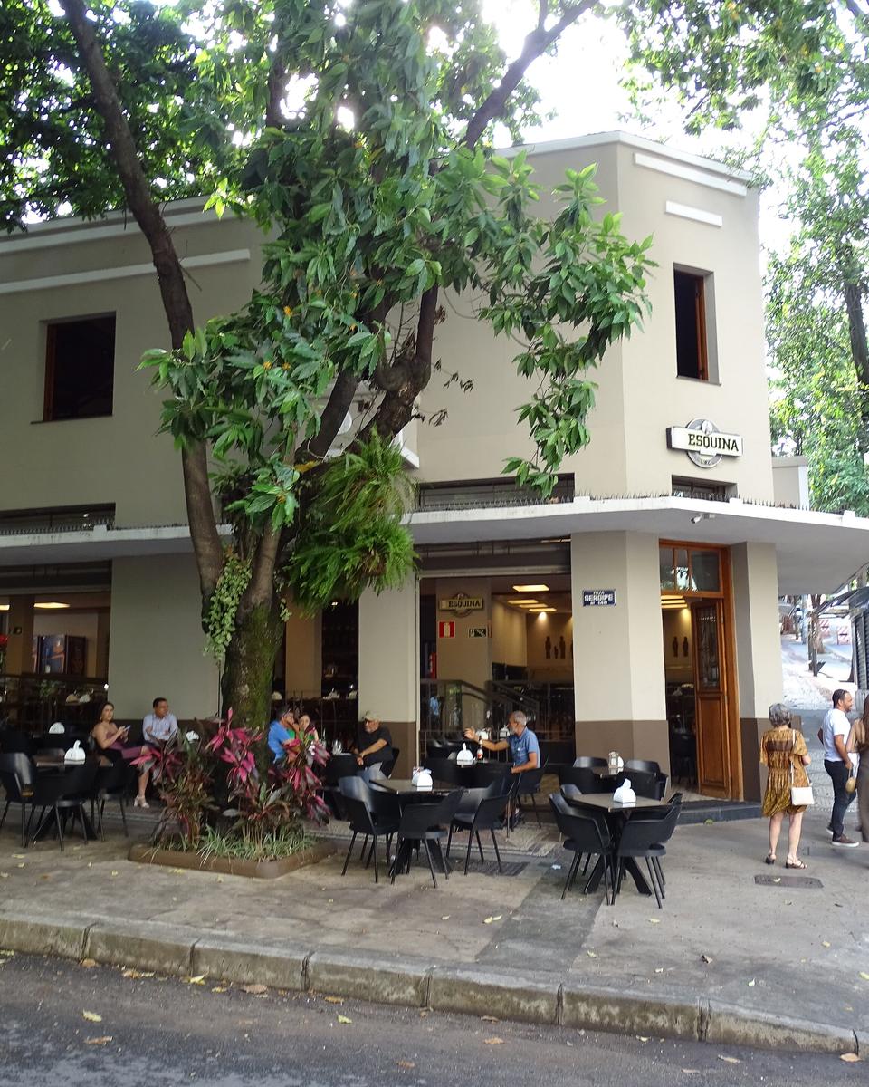 Clientes sentados em mesas na calçada do Bar da Esquina, na esquina das ruas Sergipe e Timbiras, em Belo Horizonte, sob árvores, com pessoas conversando em pé na frente do bar.