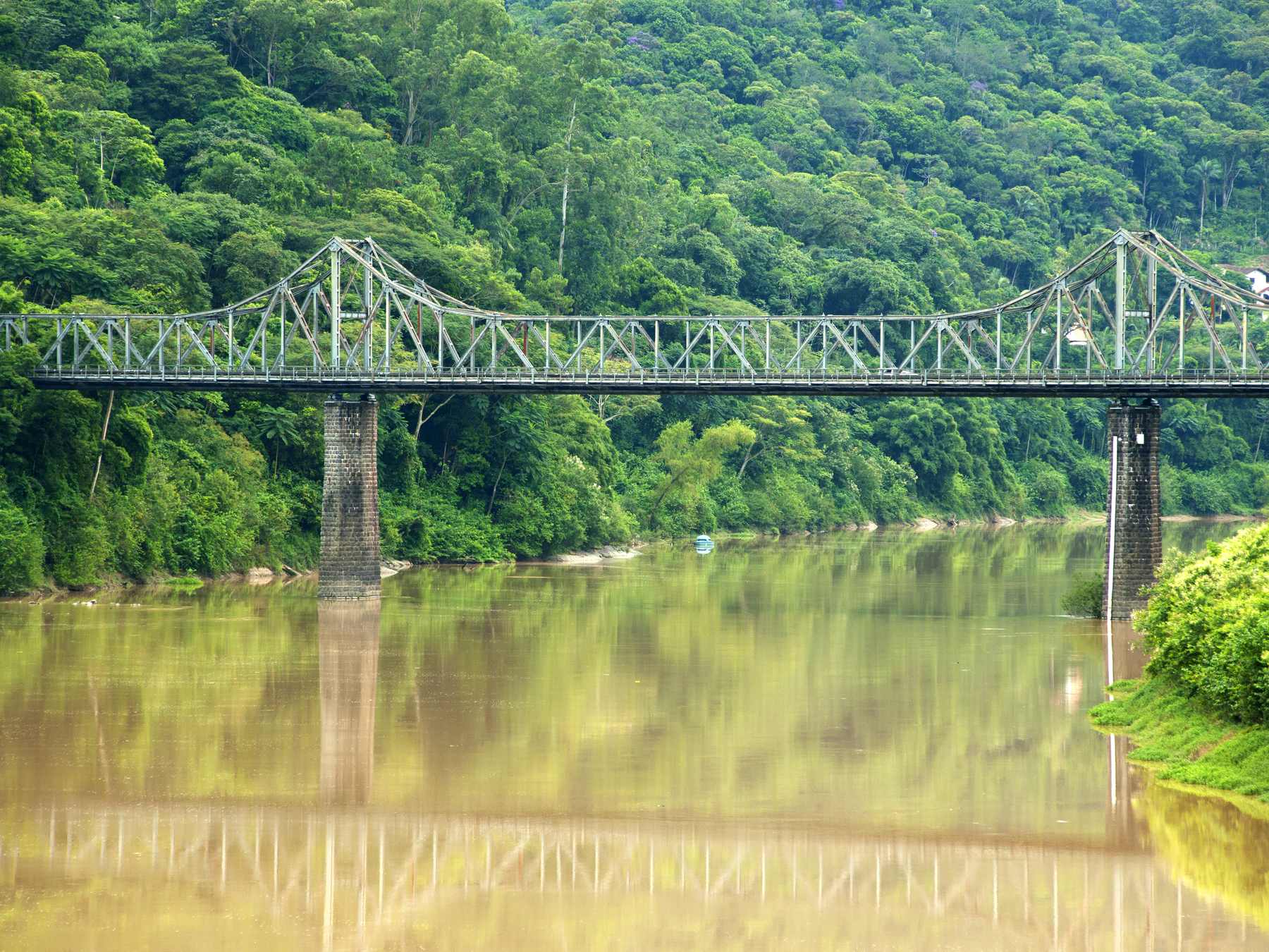 Ponte de Ferro, de estrutura metálica verde, atravessando o rio Itajaí-Açu em Blumenau, com a água refletindo a ponte e a encosta coberta de mata atlântica ao fundo.