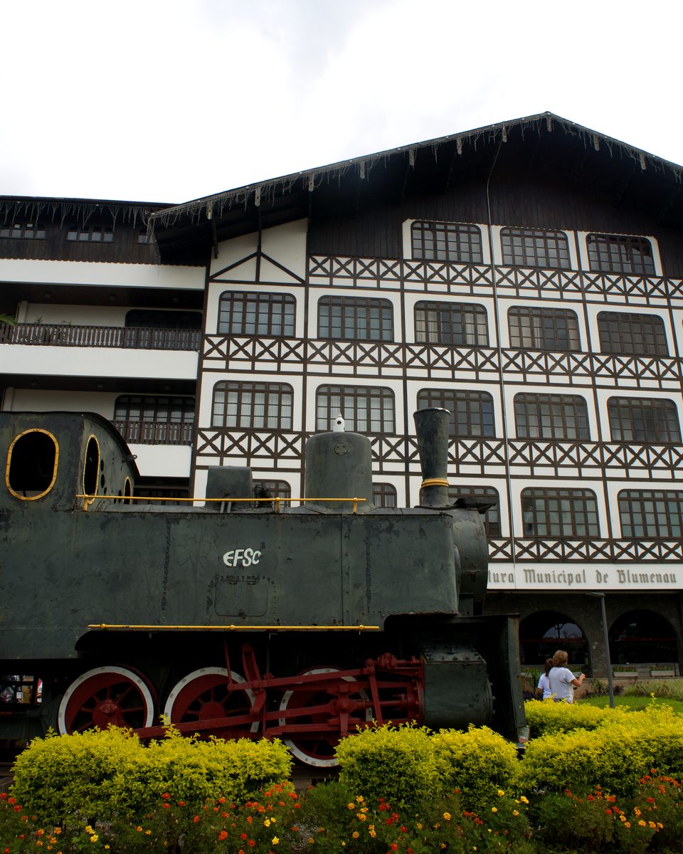 Prefeitura de Blumenau, de fachada enxaimel, com a locomotiva Macuca exposta no jardim.