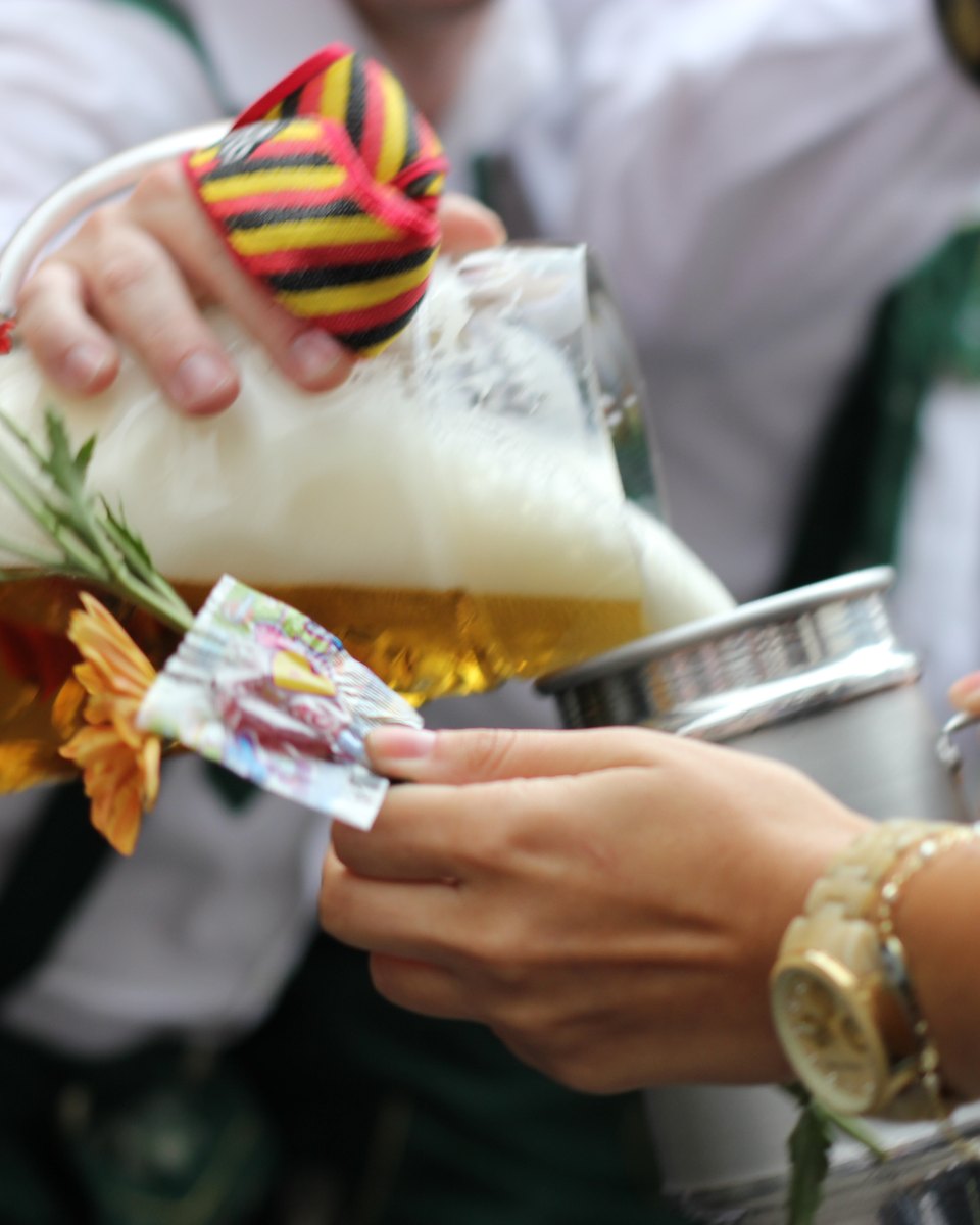 Caneca de chope com espuma, enfeitada com flores, passando de mão em mão num desfile em Blumenau.