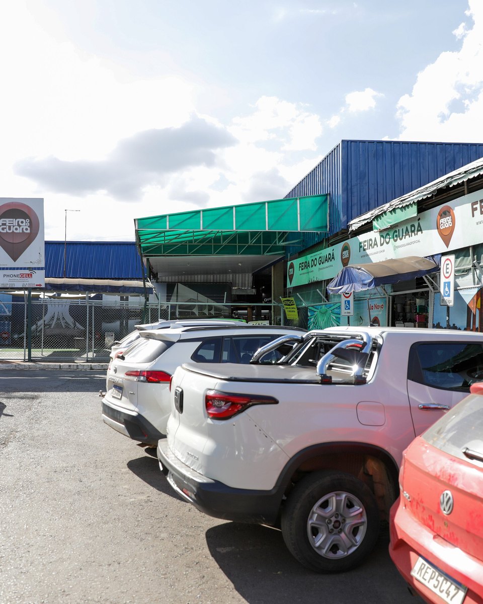Entrada da Feira do Guará, no Distrito Federal, com o letreiro da feira no alto da fachada, lojas de cada lado e carros estacionados em frente.