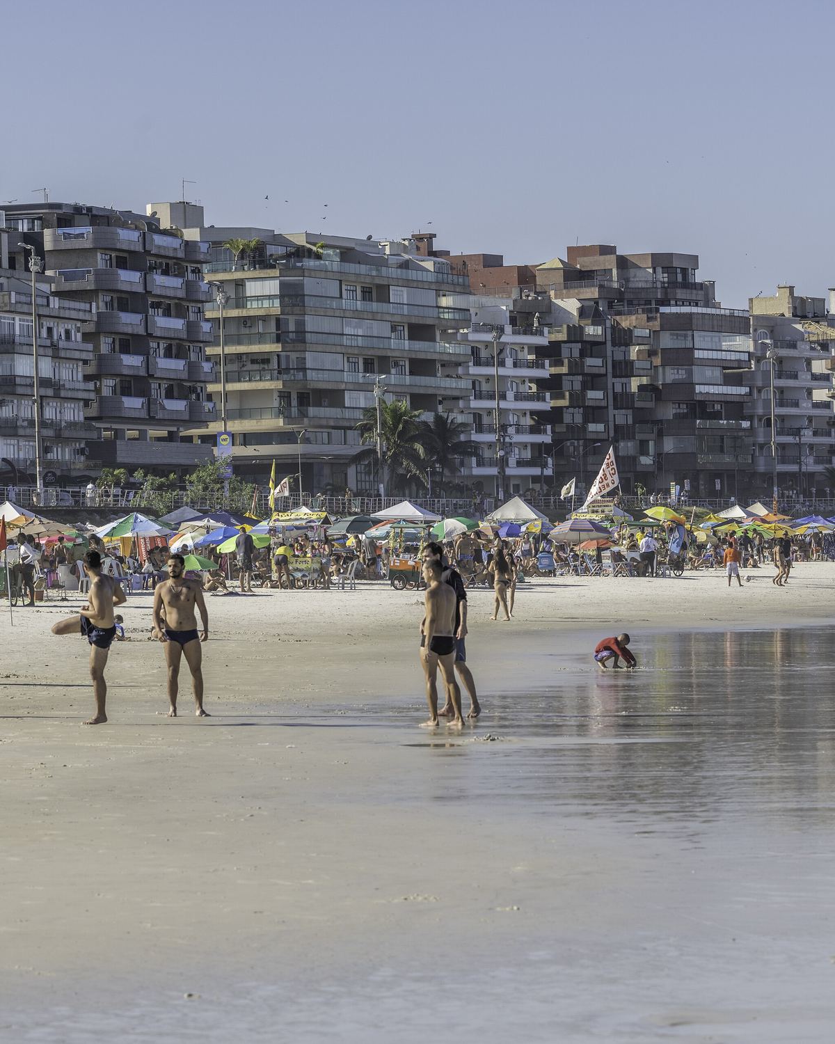 Banhistas na Praia do Forte, em Cabo Frio, com guarda-sóis e prédios da orla ao fundo.