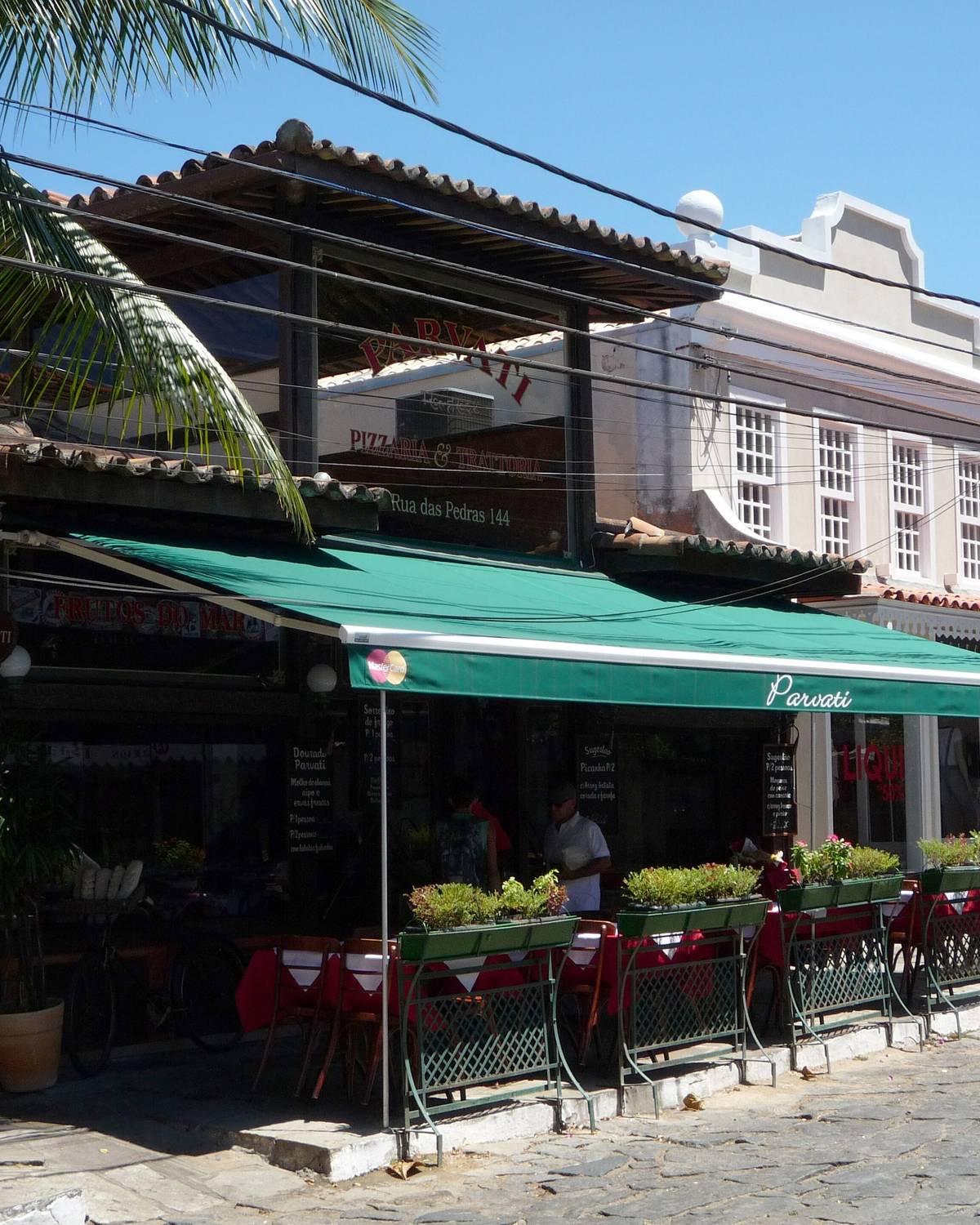 Restaurante com toldo verde e mesas na calçada da Rua das Pedras, em Búzios.