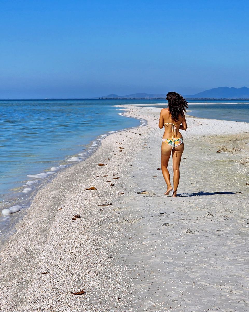Mulher de biquíni caminhando por uma faixa de areia branca na Lagoa de Araruama, em Arraial do Cabo.