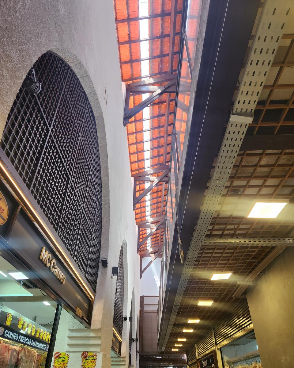 Corredor interno do Mercado Municipal de Campinas, com arcos brancos, telhado de madeira e lojas de comida.