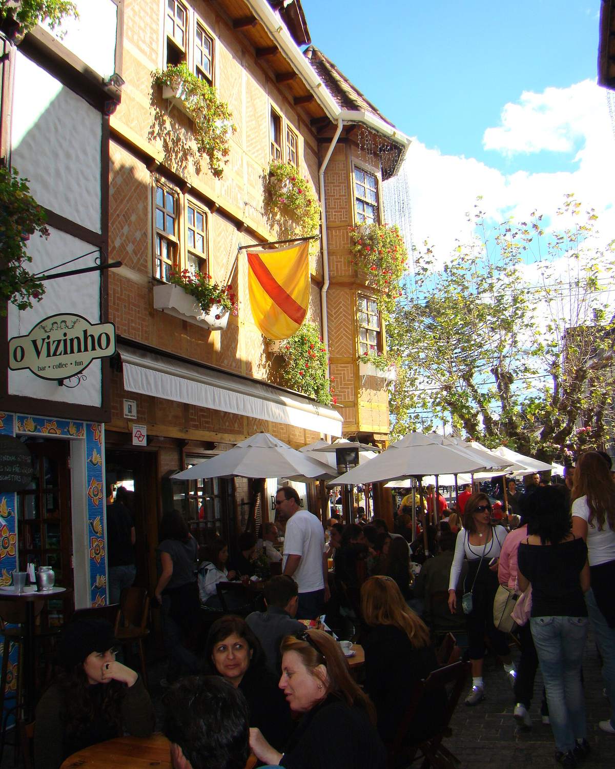 Turistas de casaco nas mesas de restaurantes de uma rua de pedestres da Vila Capivari, entre casas de estilo europeu com floreiras.