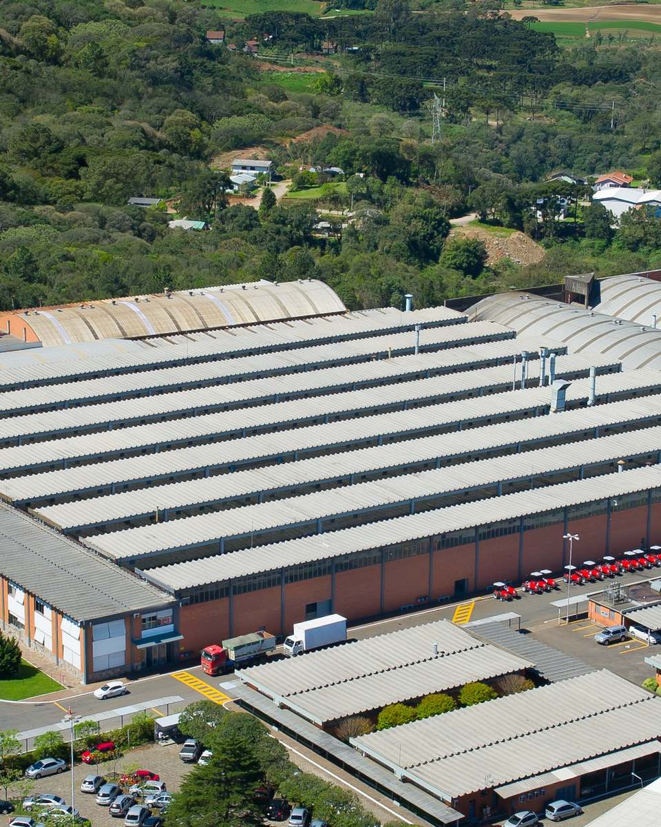 Vista aérea de um pavilhão industrial em Caxias do Sul, cercado de árvores.