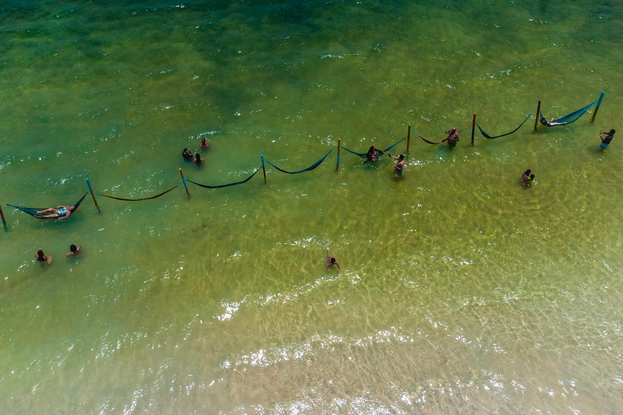 Vista aérea da Lagoa do Paraíso, perto de Jericoacoara, com a água verde-clara e uma fileira de redes armadas dentro da lagoa, com pessoas deitadas e em pé na água rasa.