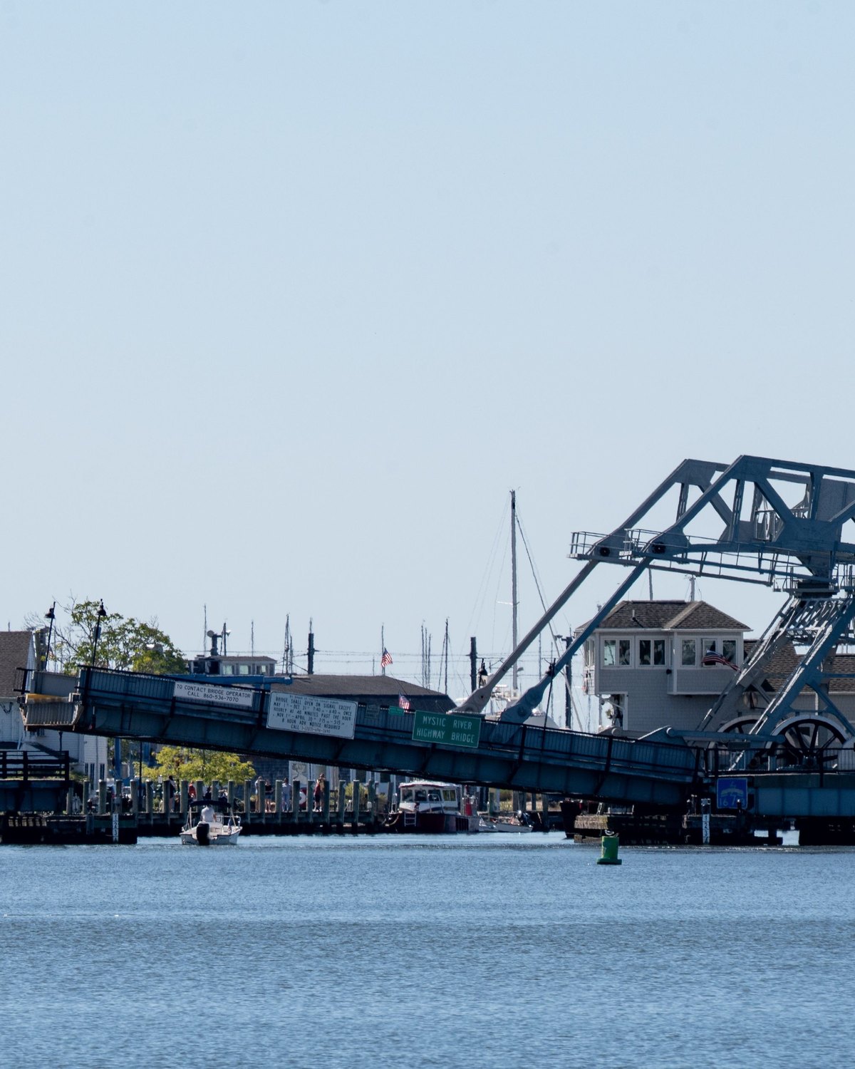 Veleiro de vela vermelha no rio Mystic, diante da ponte levadiça de ferro azul e das casas da beira do rio.