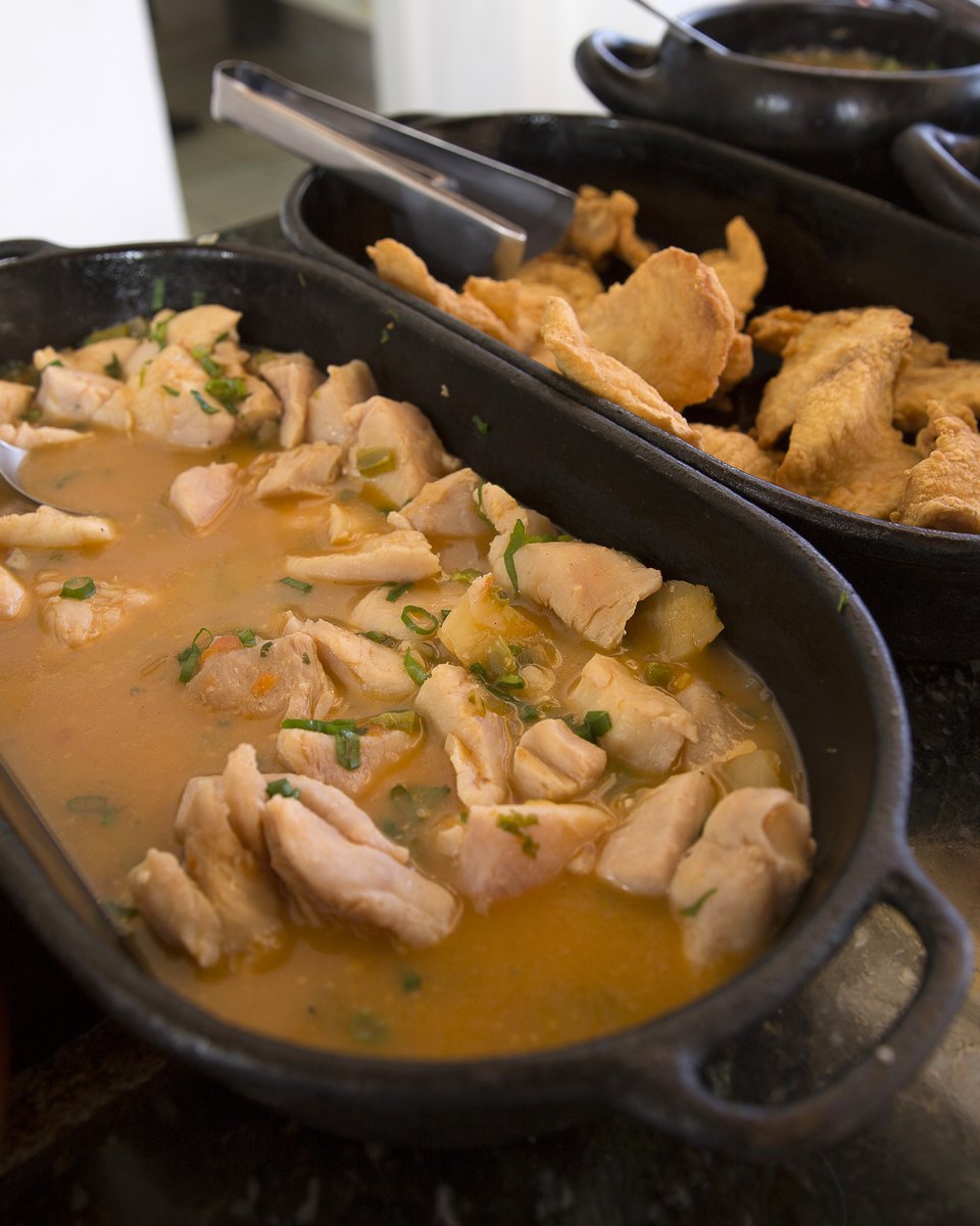 Panelas de ferro com peixe ensopado, peixe frito e acompanhamentos sobre o balcão de um restaurante de comida regional em Cuiabá.
