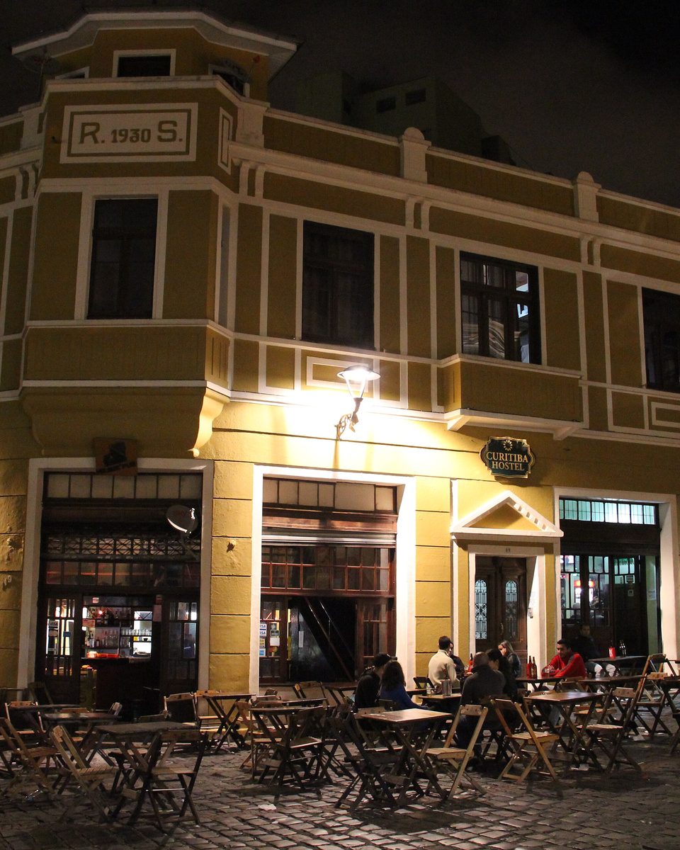 Mesas na calçada de um bar num casarão do Largo da Ordem, em Curitiba, à noite.
