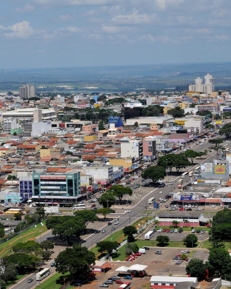 Vista do alto de Ceilândia, com quadras de casas e prédios baixos a perder de vista, avenidas largas, comércio e árvores em primeiro plano.