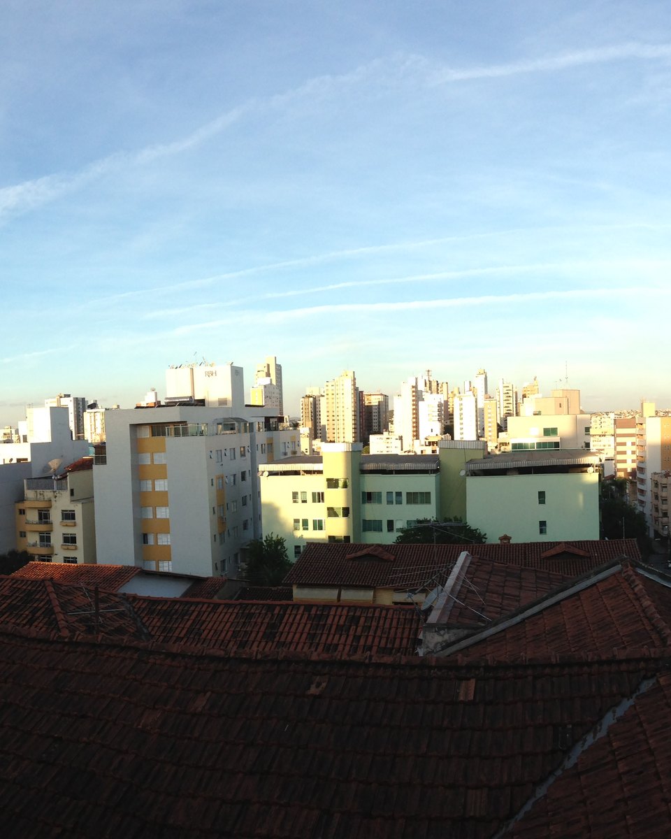 Panorama do Centro de Divinópolis, com prédios residenciais e comerciais sob o céu claro e um telhado de cerâmica em primeiro plano.