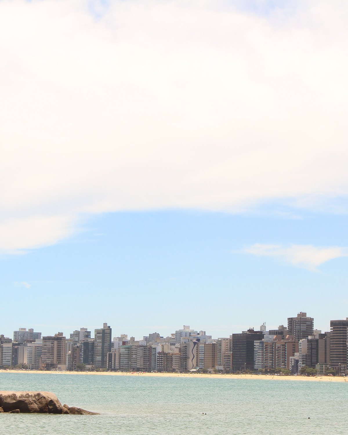 Praia da Costa vista do mar, com a faixa de areia e os prédios de Vila Velha na linha do horizonte.