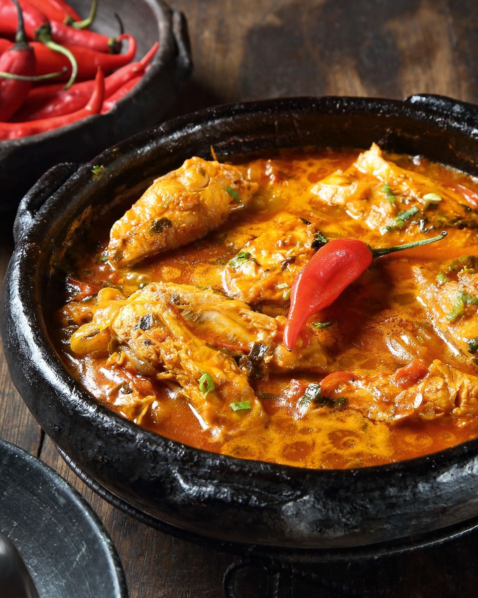 Moqueca capixaba de peixe servida na panela de barro preta, com pimentas ao lado sobre a mesa de madeira.