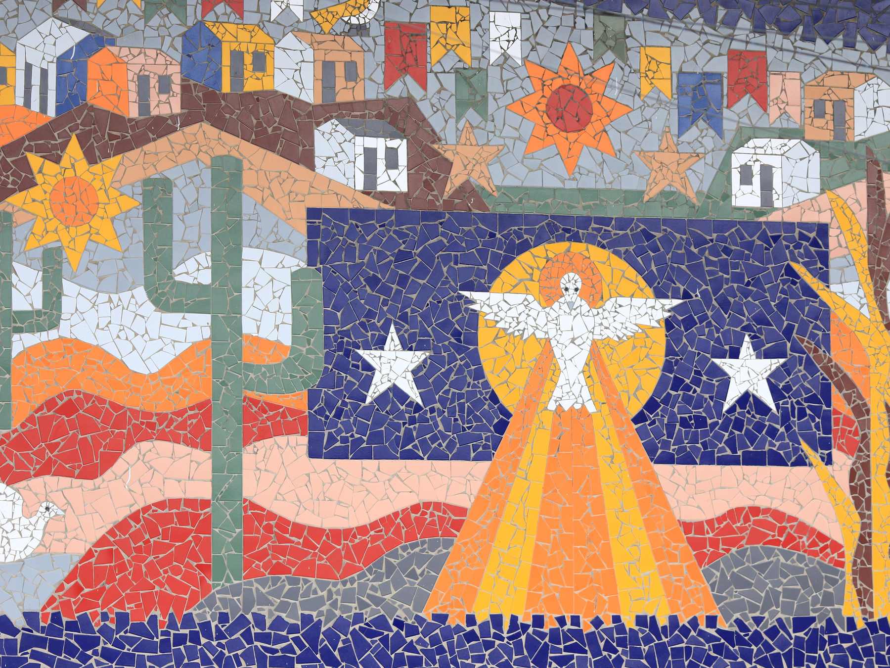 Detalhe do painel de mosaico O Divino e o Sertão, de Juraci Dórea, na fachada do Centro Paroquial Senhora Santana, em Feira de Santana, com a pomba do Divino num sol laranja, estrelas brancas sobre fundo azul, mandacarus, bandeirinhas de São João e casinhas coloridas.
