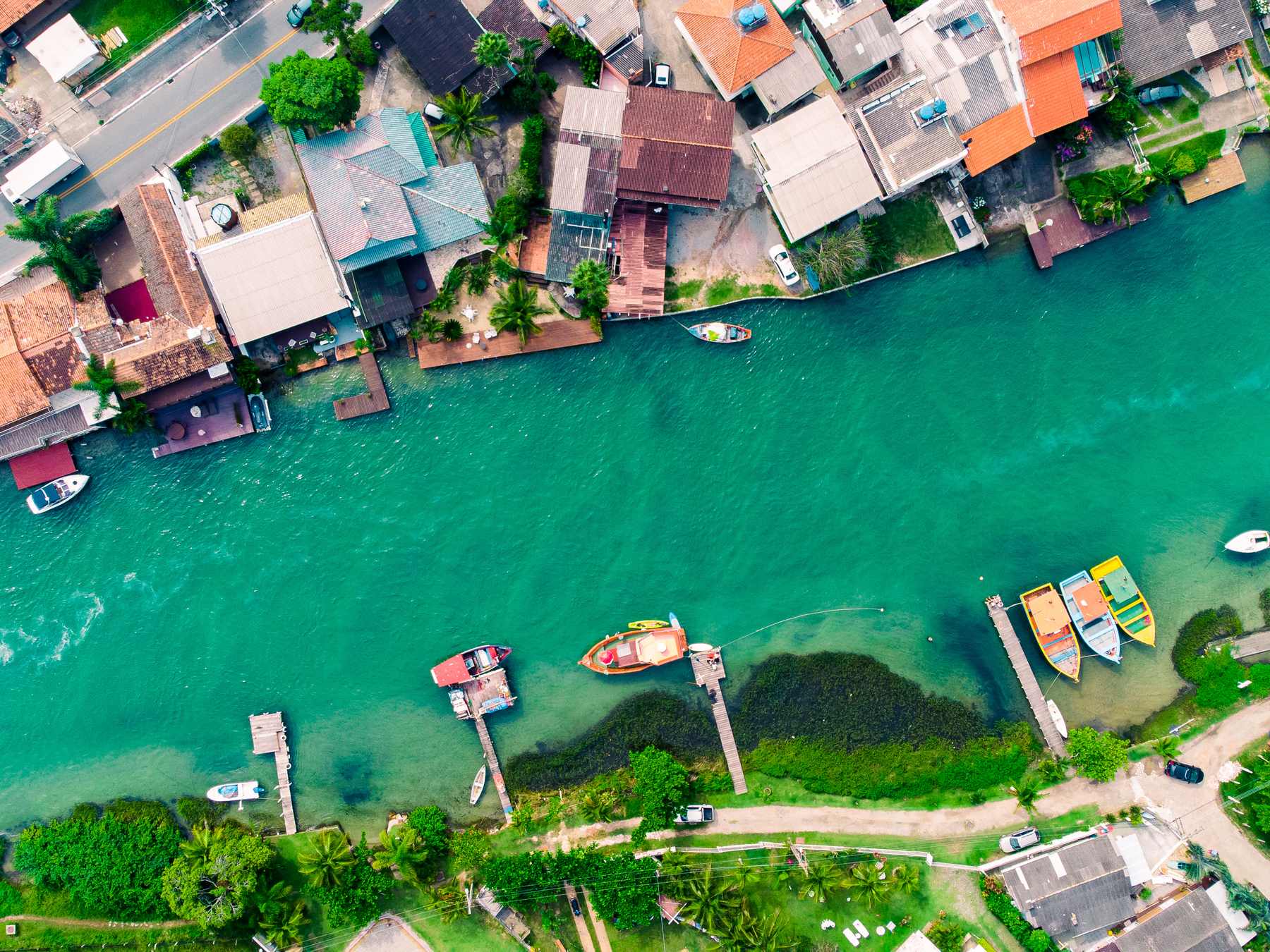 Canal da Barra da Lagoa visto de cima, com a água verde-esmeralda, barcos de pesca coloridos presos aos trapiches e as casas do bairro na margem.