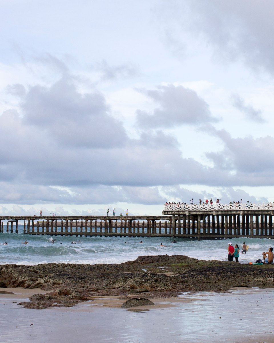 Ponte dos Ingleses e a areia da Praia de Iracema, em Fortaleza, com pessoas nas pedras.