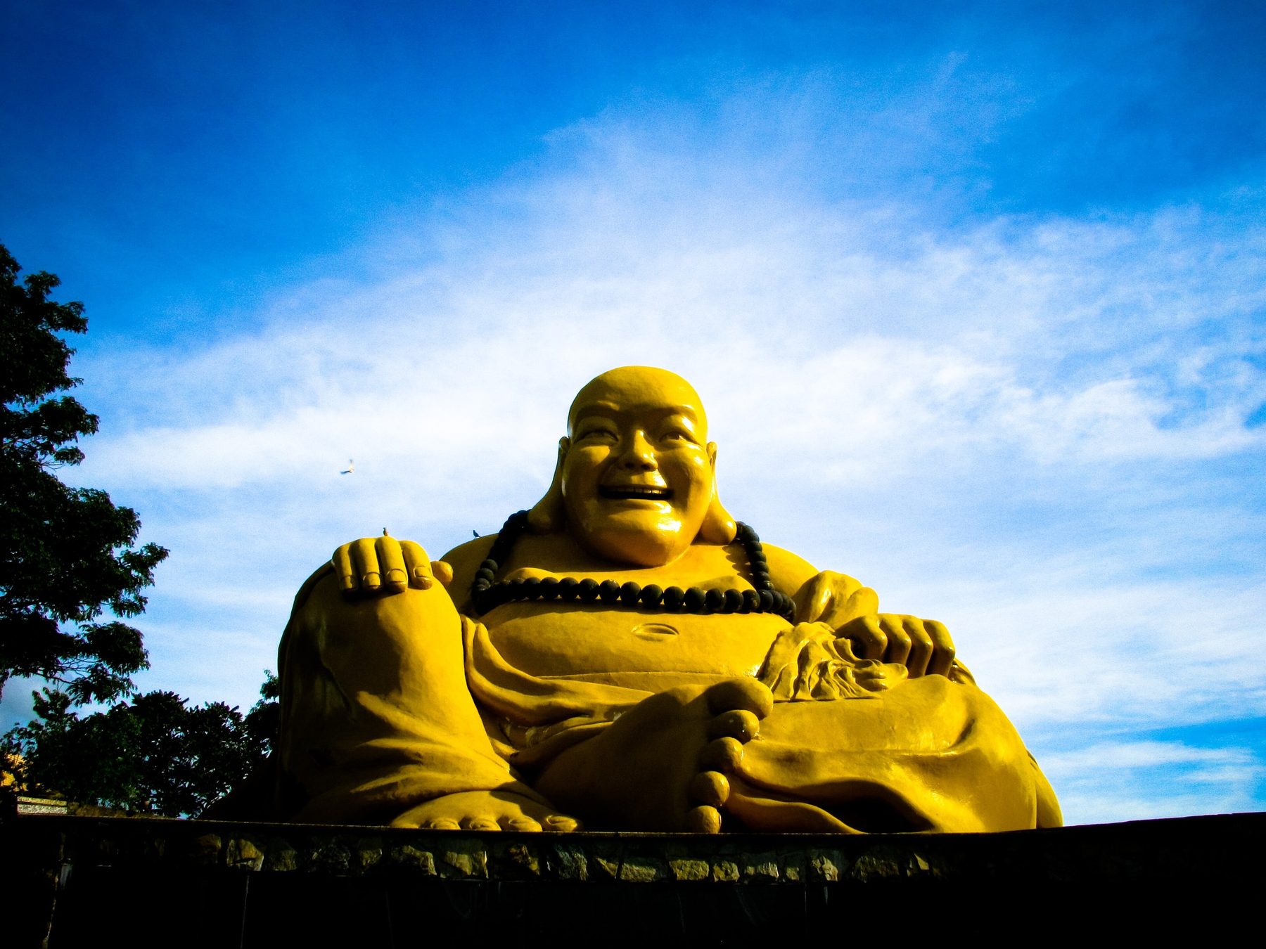 Estátua amarela gigante de um Buda sorridente sentado, contra o céu azul com nuvens, no Templo Budista Chen Tien.