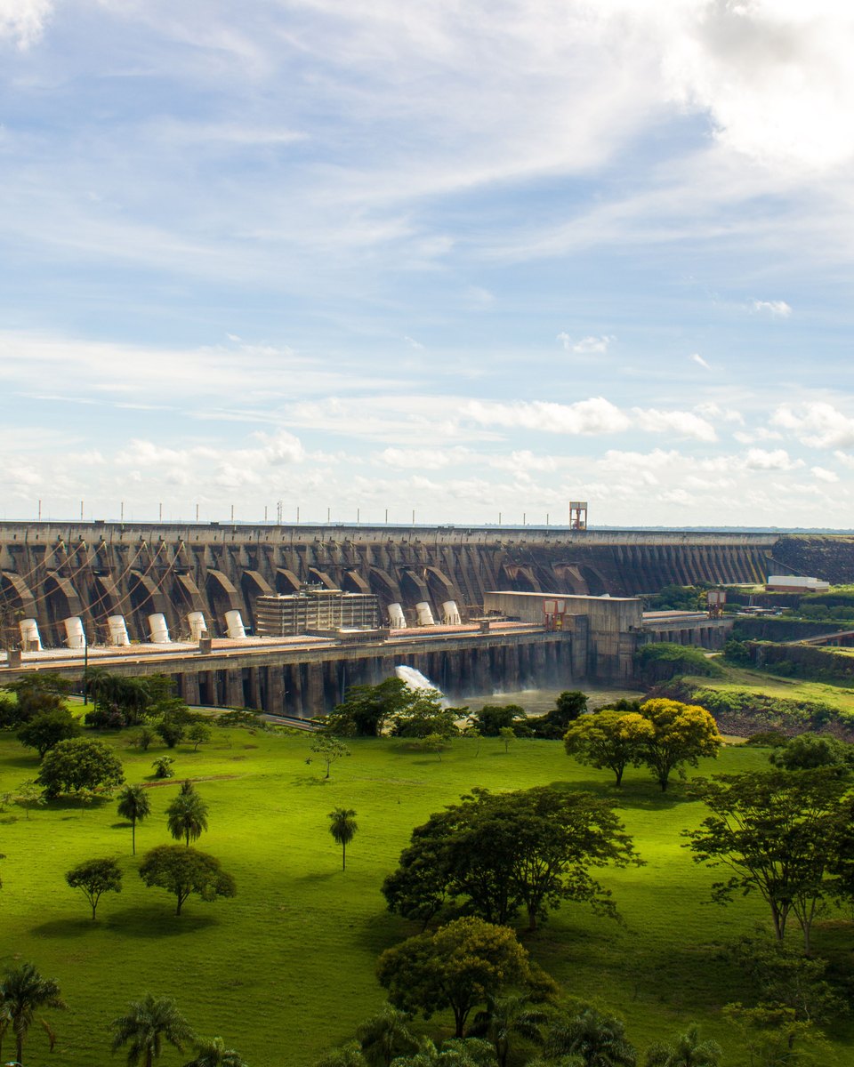 Barragem de Itaipu vista do mirante, com o gramado e as palmeiras em primeiro plano.