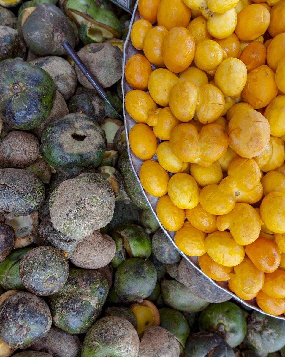 Pequis inteiros de casca verde e escura ao lado de uma bacia cheia de caroços de pequi amarelos já descascados, à venda no Centro de Goiânia.